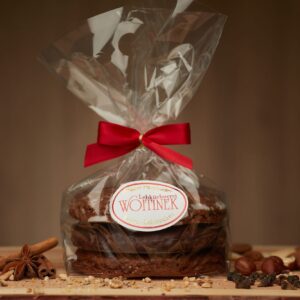 Drei Schokoladenkuchen von Lebkuchenerei Wottinek, verpackt mit roter Schleife auf Holzbrett mit Gewürzen