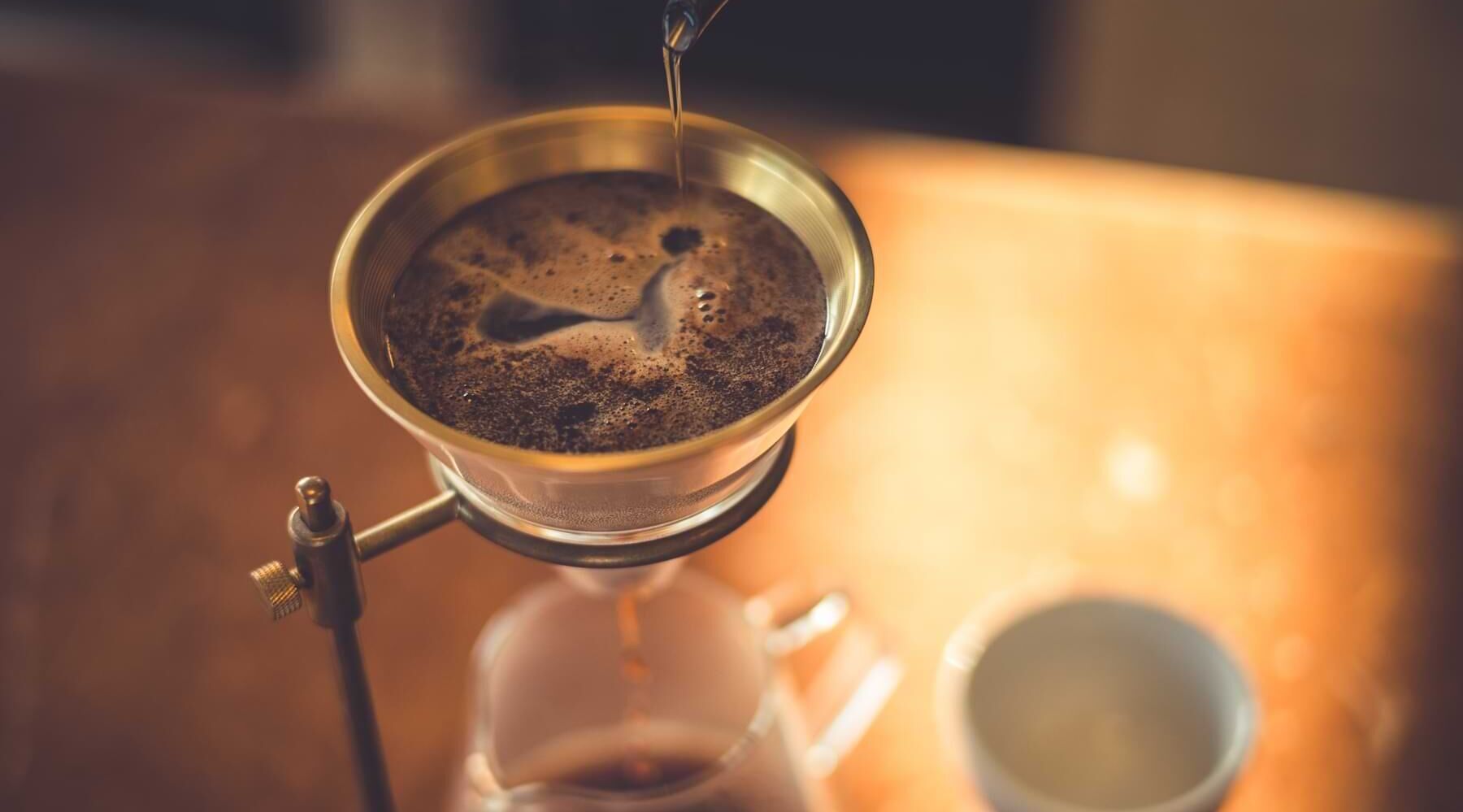 Kaffee wird durch einen Metallfilter in eine Glaskaraffe gebrüht, daneben steht eine leere Tasse